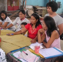 Several women and children gather around a table to make posters