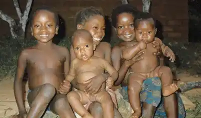 A group of five happy young children sitting down and smiling after being treated successfully for scabies.