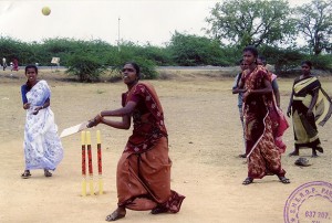 A woman holding a bat looks in the air as a ball comes towards her.