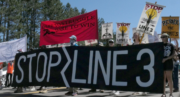 Group of people march in protest and hold a banner supporting Stop Line 3.