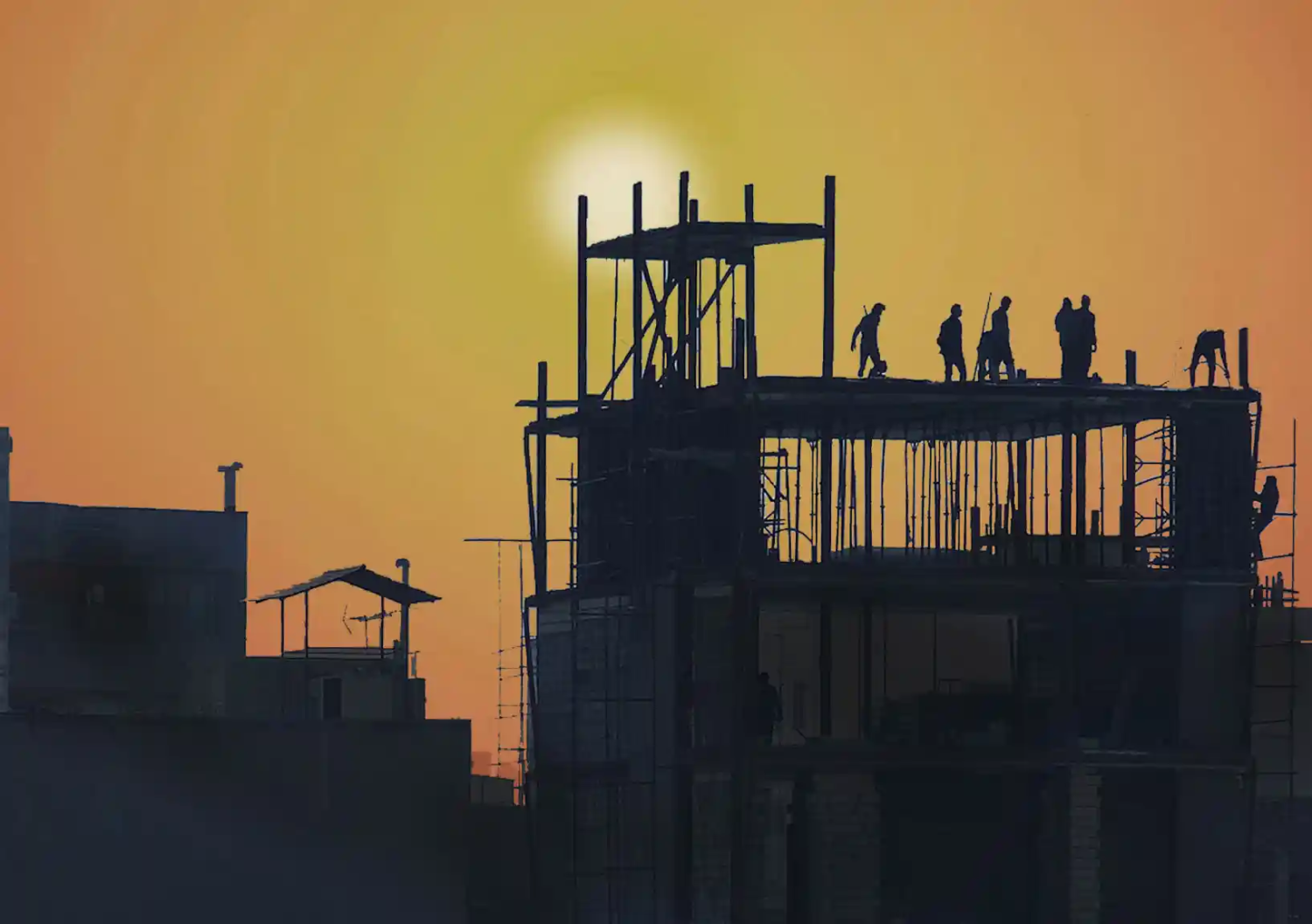 Construction workers work hard on a building site as the sun hovers over.