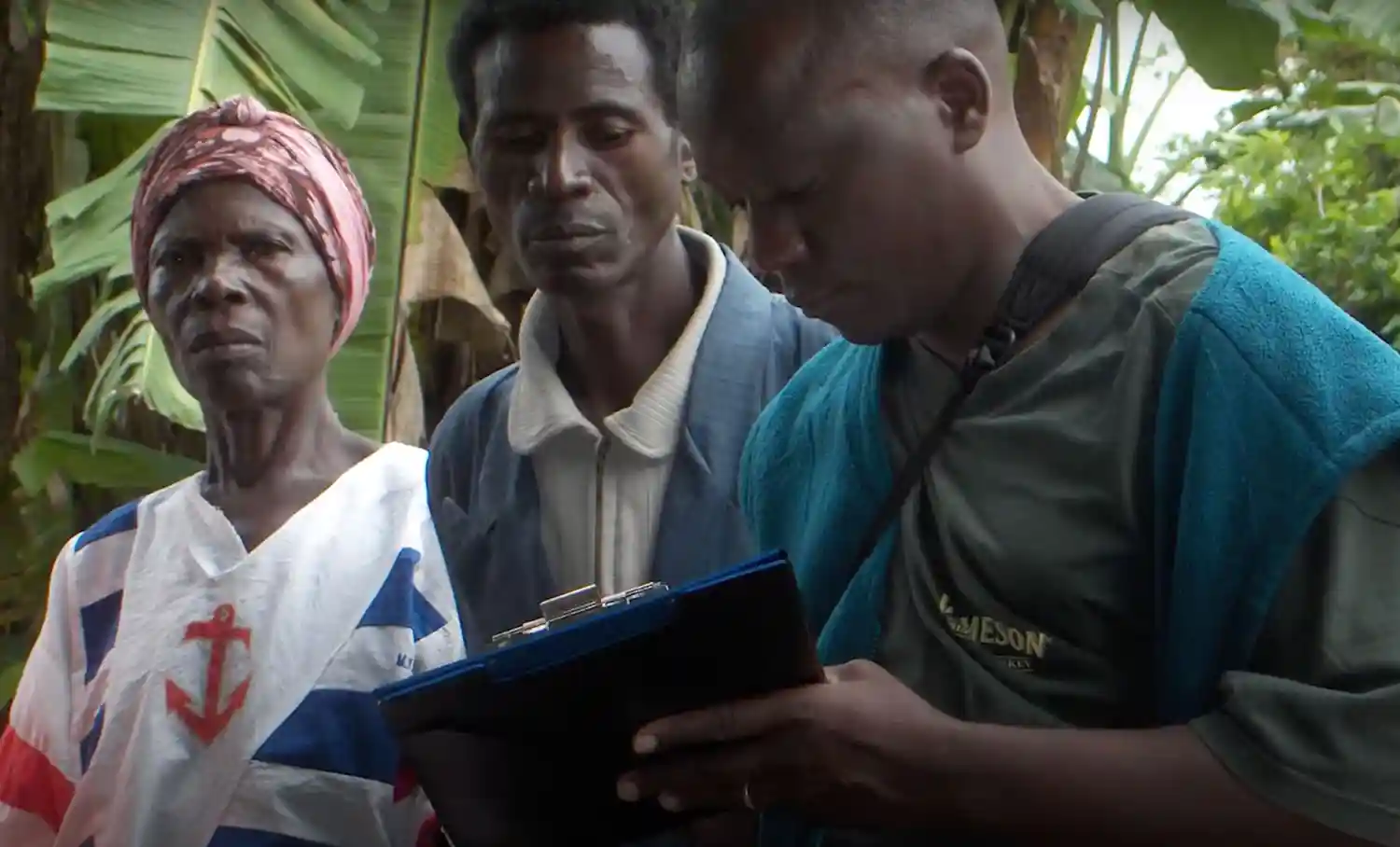 A health worker is writing on a clipboard while asking questions to a man and woman beside him.