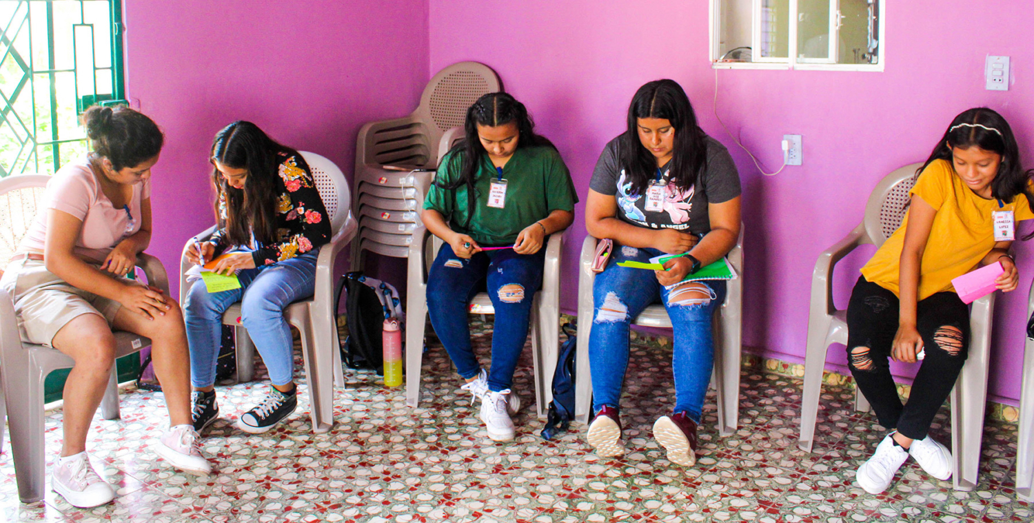 A group of Salvadorean teens work together on a learning activity in a brightly painted room." title="A group of Salvadorean teens work together on a learning activity in a brightly painted room.