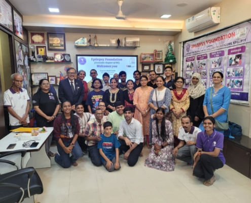 a group photo of men, women, and children in a meeting room. They stand in front of a screen that reads "Epilepsy Foundation Welcomes You"