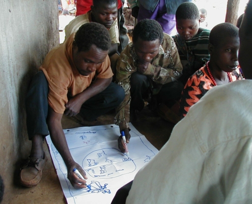 A group of African men gather around a large paper. Two of them make notes on the paper with markers.